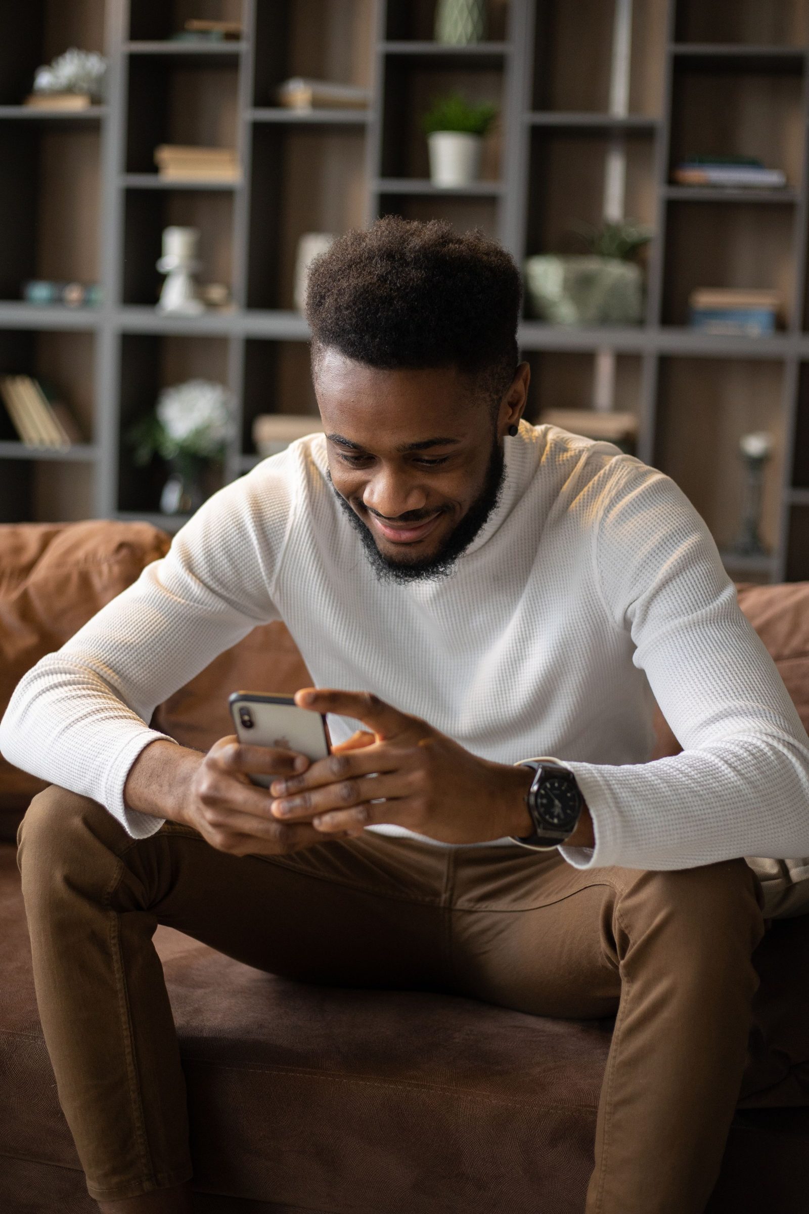 A man relaxing on the sofa at home, smiling at his phone