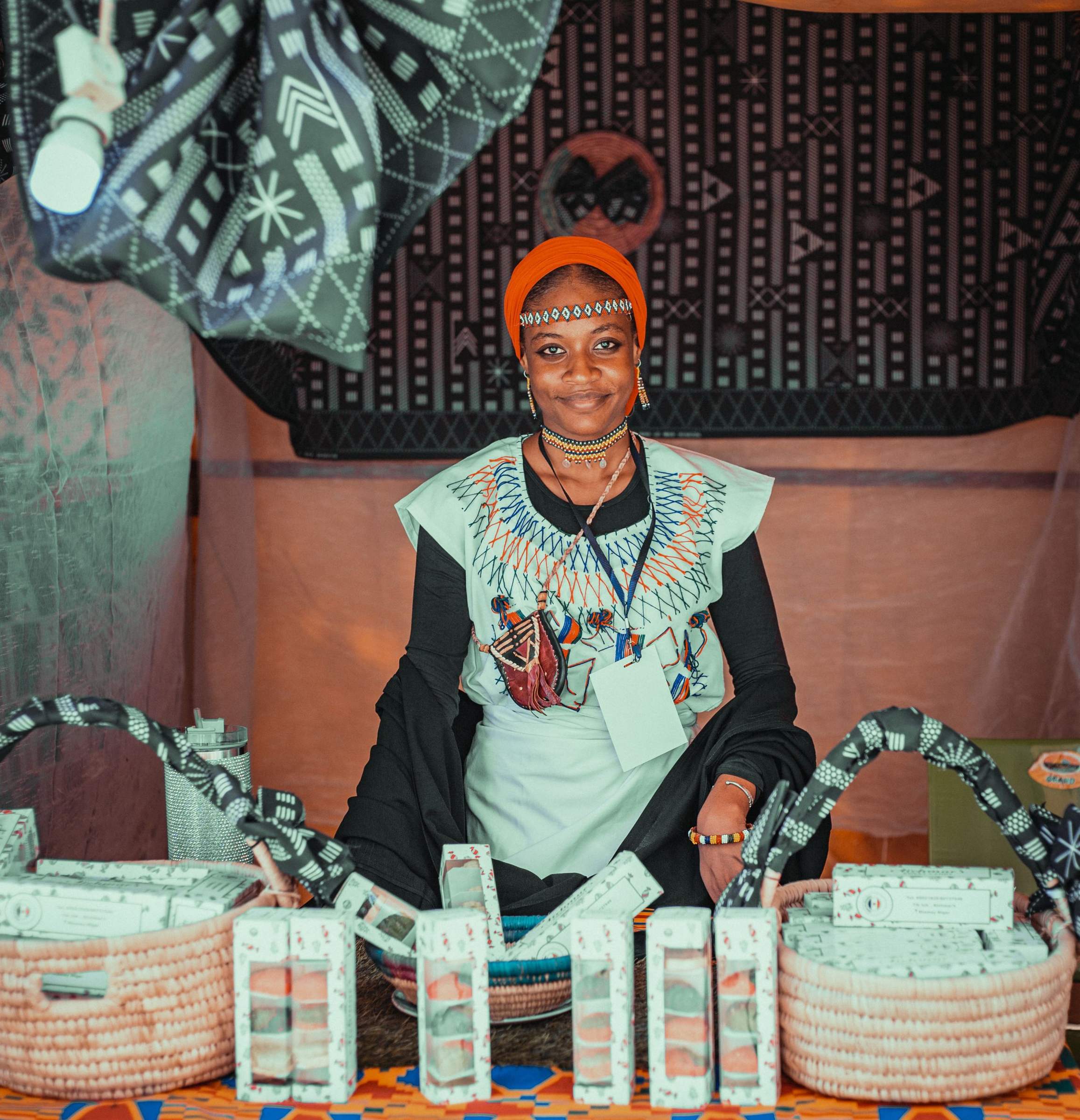 A smiling artisan behind her market stall of handmade baskets
