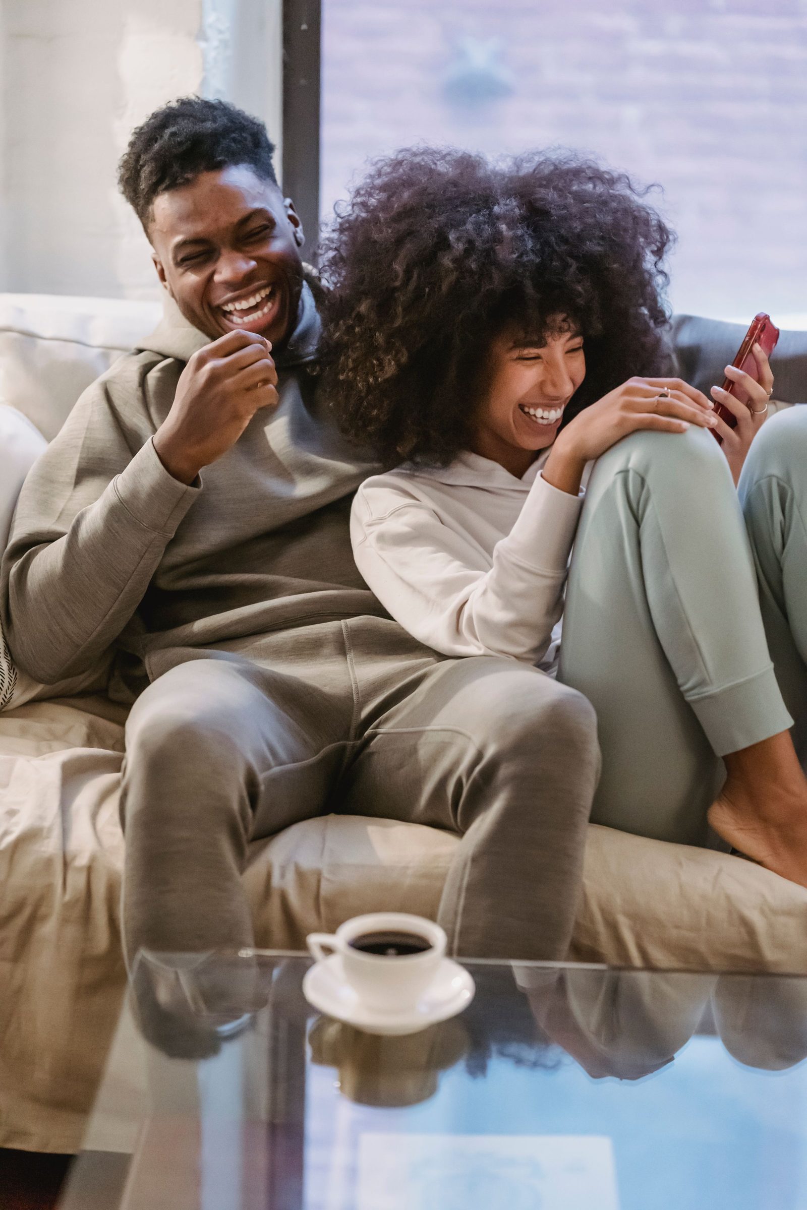 Two housemates laughing together on the sofa over a phone